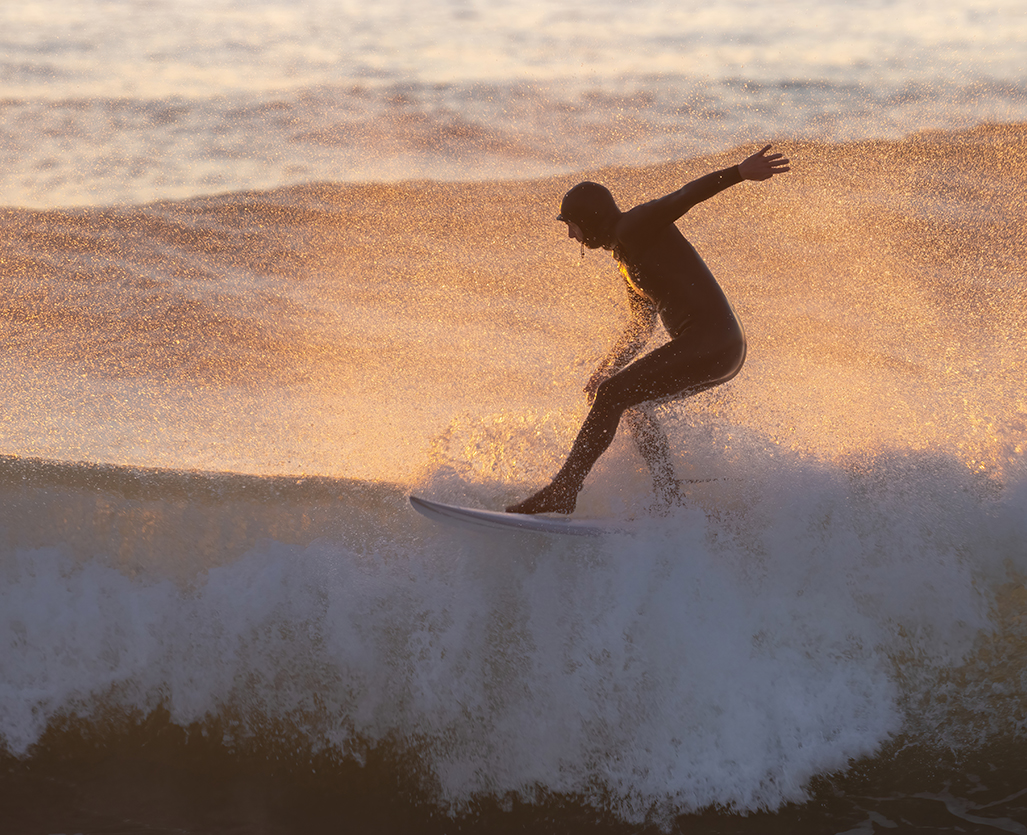 Surfer riding waves at sunset with golden light over the Cornwall coast