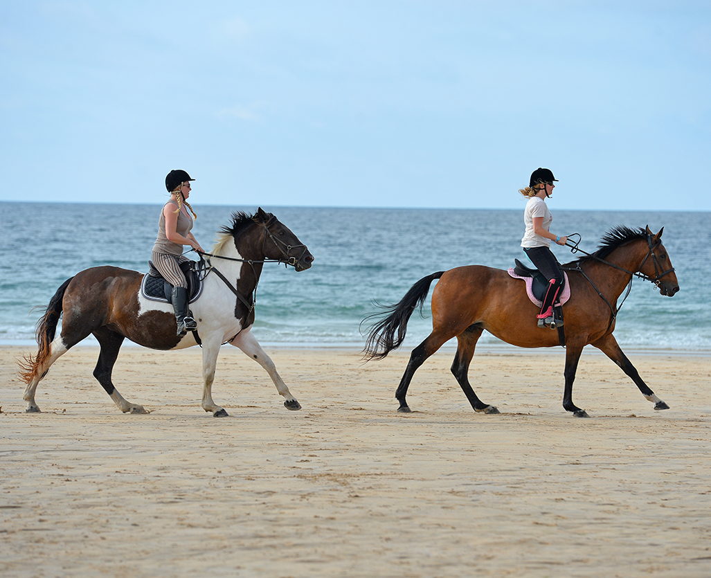 Horse riders galloping along a sandy beach on the Cornwall coast