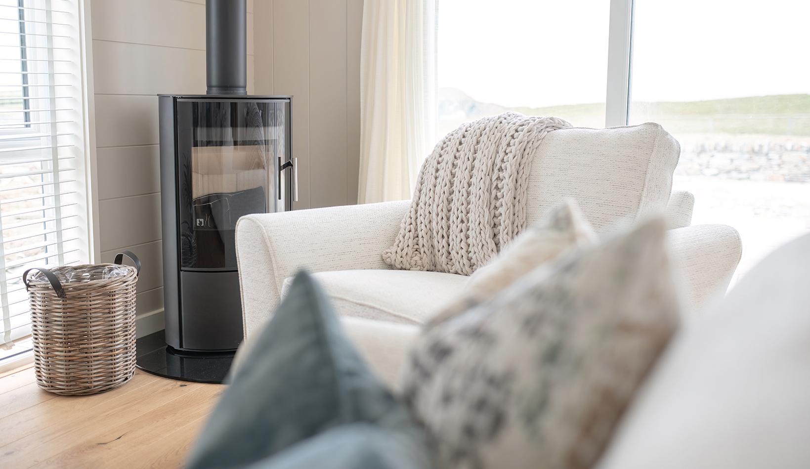 Comfortable reading nook with a wood-burning stove, armchair and textured knitted blanket.